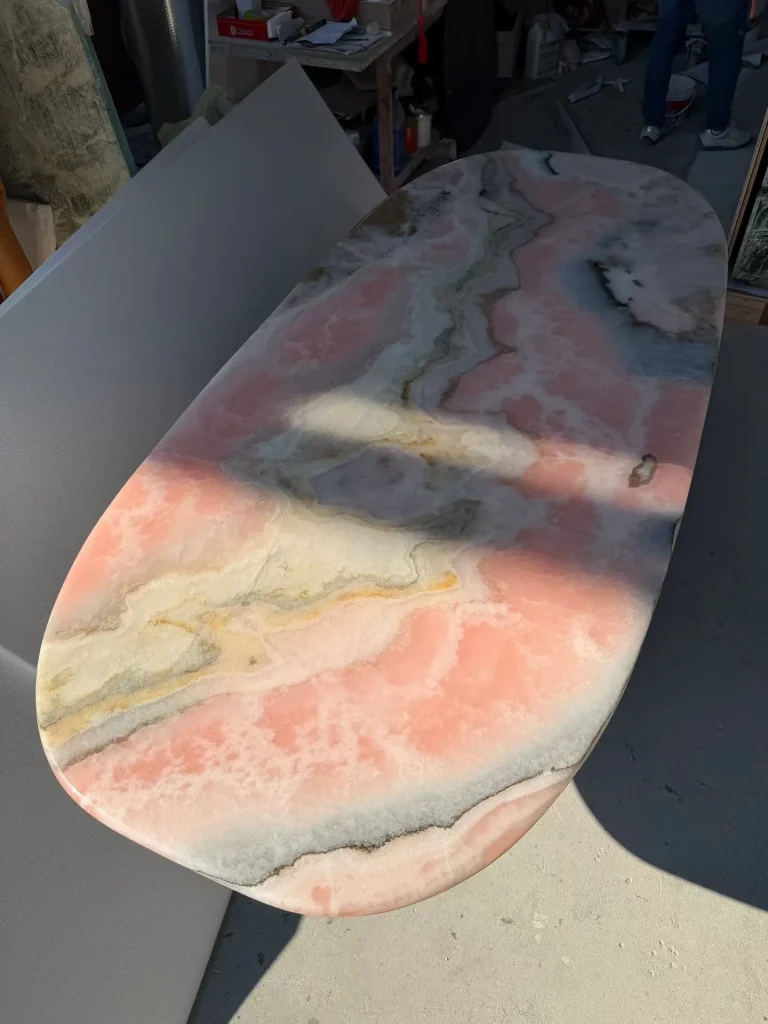 rose-red stone dining table, with an oval top and cloudy mottling, in a workshop