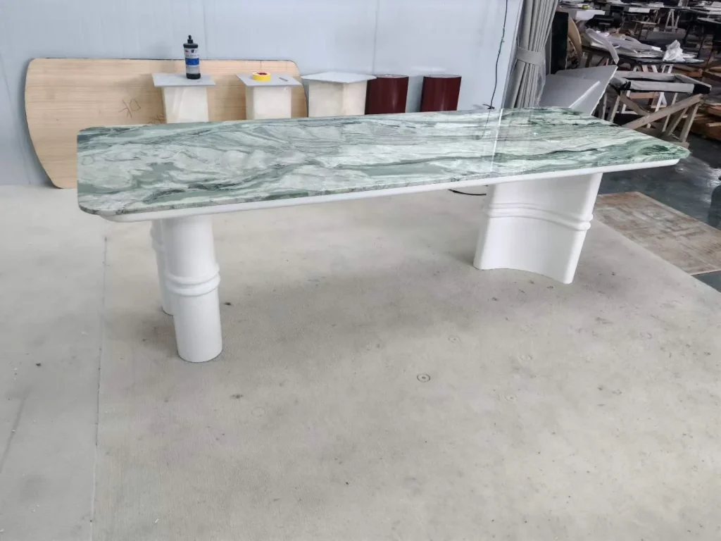white stone dining table, with bold veining, showing a single main form with workshop equipment nearby