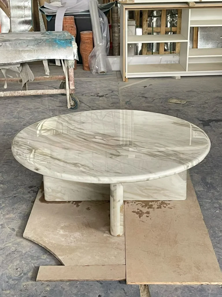 white stone coffee table, with a round top and fine veining, in a workshop