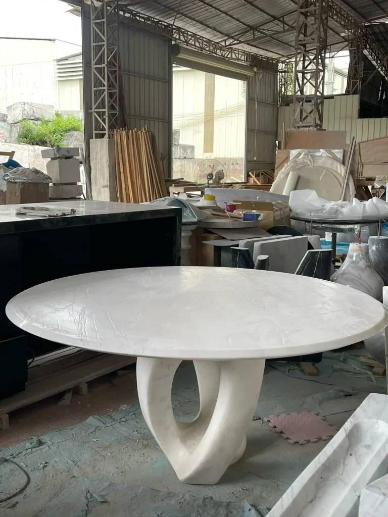white stone dining table, with a round top and fine veining, in a workshop